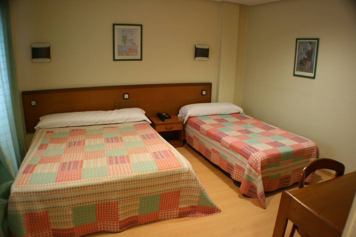 Habitación doble con dos camas, cabecero de madera, mesitas de noche y una silla de madera.