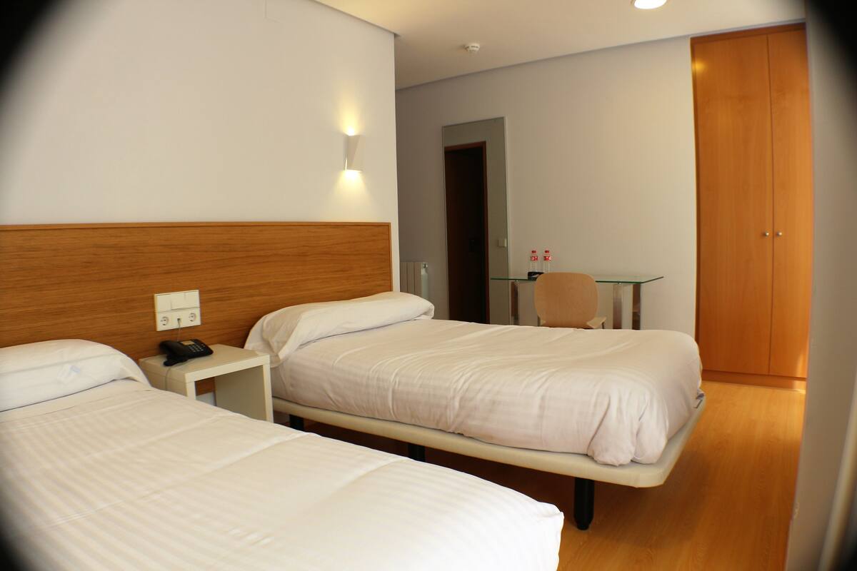 Una habitación de hotel con dos camas, una mesita de noche con teléfono, un espejo y un armario de madera.