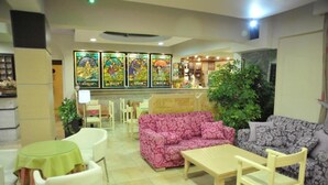 A hotel lobby with a bar area, two patterned sofas, a wooden table, and a green table with a chair. - Anseli Hotel Apartments and Studios (Rhodes)