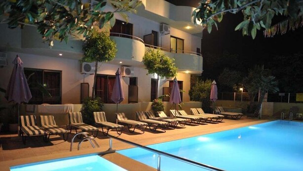 A swimming pool with lounge chairs and umbrellas, surrounded by a building with balconies and air conditioning units. - Anseli Hotel Apartments and Studios (Rhodes)