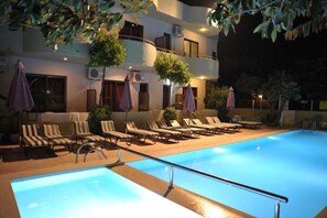 Zwembad met ligbedden en parasols, omringd door een gebouw met balkons en airconditioners.