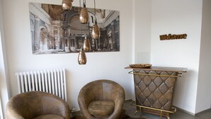 A room with two brown leather armchairs, a white round table, a tufted metal sideboard, a 'Welcome' sign, and a large classical-style painting on the wall. - Hotel Central Wesseling (Wesseling)