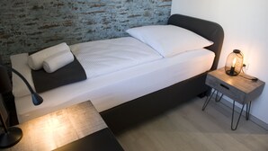 A neatly made bed with white linens and a black headboard, a bedside lamp, and a small wooden nightstand with a lamp. - Hotel Central Wesseling (Wesseling)