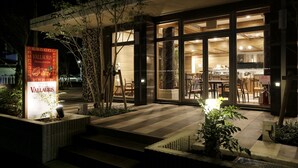 Un edificio moderno con un restaurante llamado Vallauris. Cuenta con puertas de cristal grandes, una entrada con azulejos y terraza al aire libre con plantas.