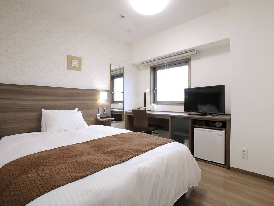 A hotel room with a bed, a desk, a television, and a refrigerator.