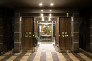 An entrance with a checkered floor, a glass door, and a small table with a plant inside.