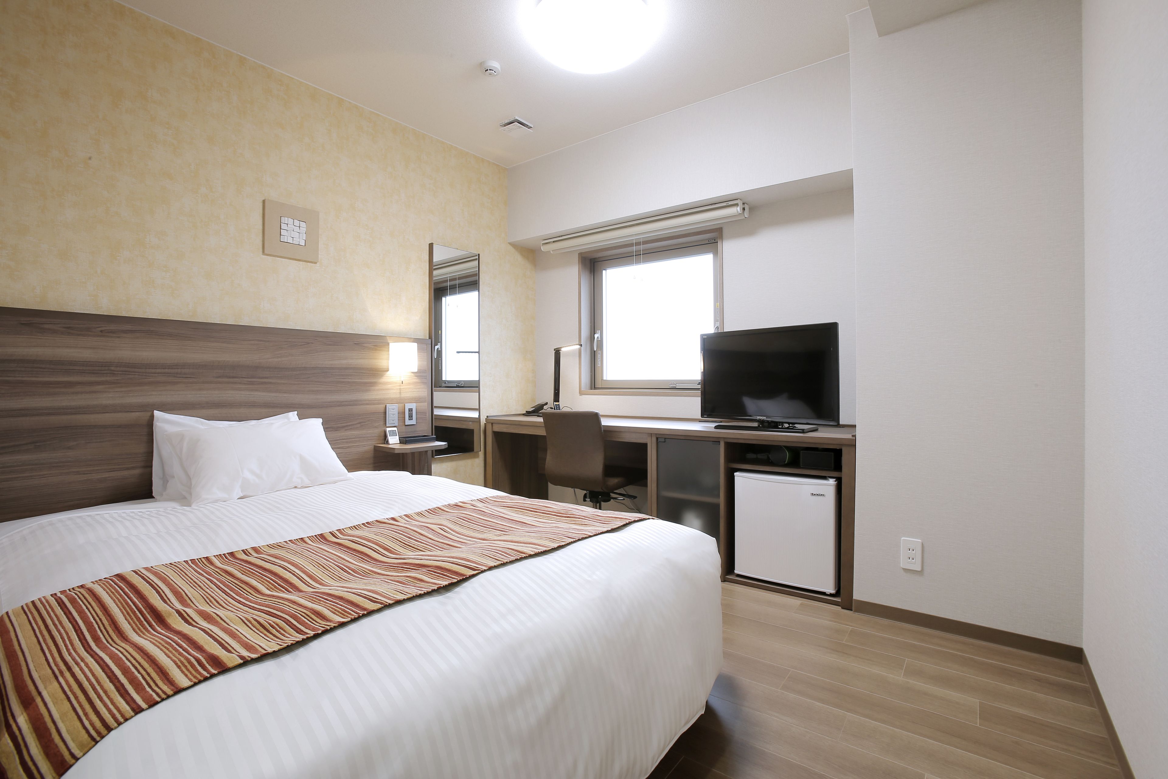 Habitació d'hotel amb un llit gran, una taula de treball amb un ordinador i una televisió.