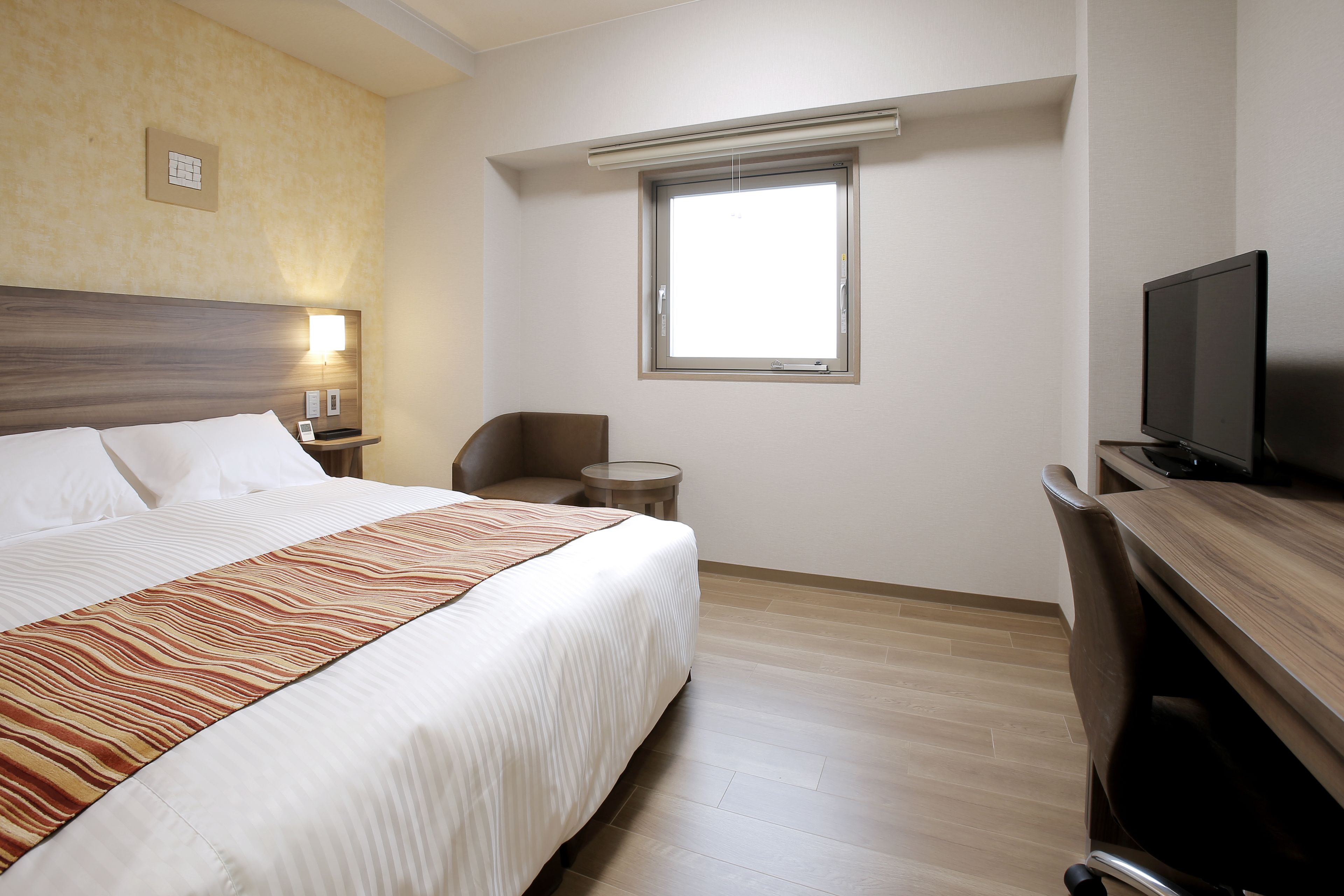 A hotel room with a bed, a TV, a desk, and a window.