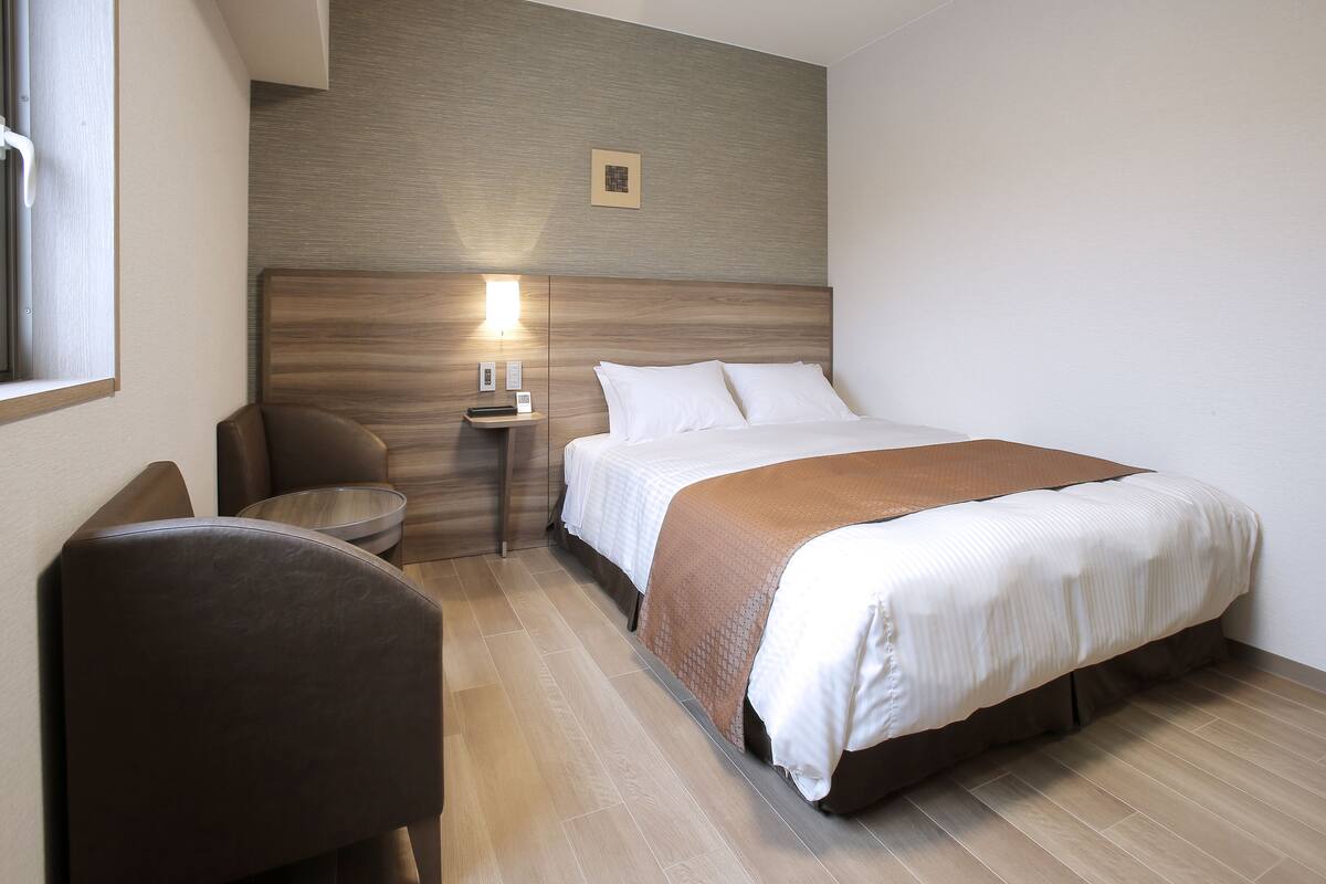 Une chambre d’hôtel comprenant un lit, une table de chevet, une chaise et une lampe fixée au mur.