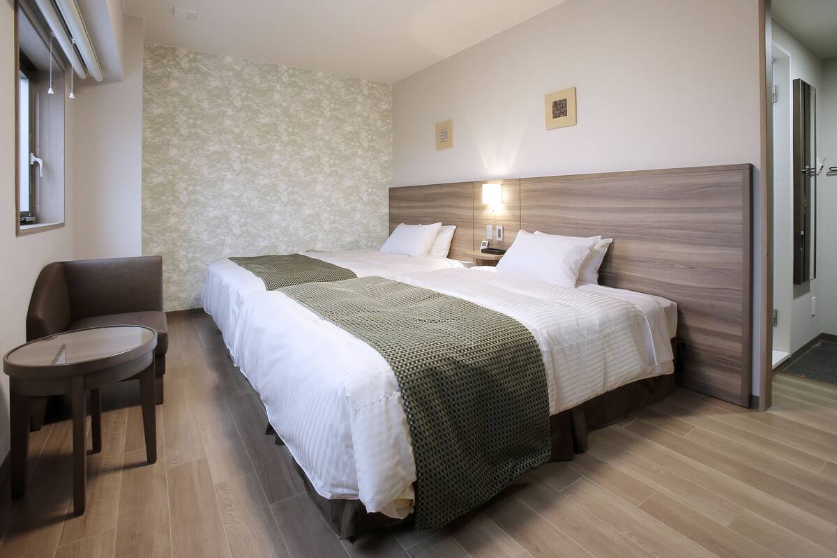 Une chambre d’hôtel avec deux lits, une petite table ronde, un canapé et un mur décoré d’un motif.