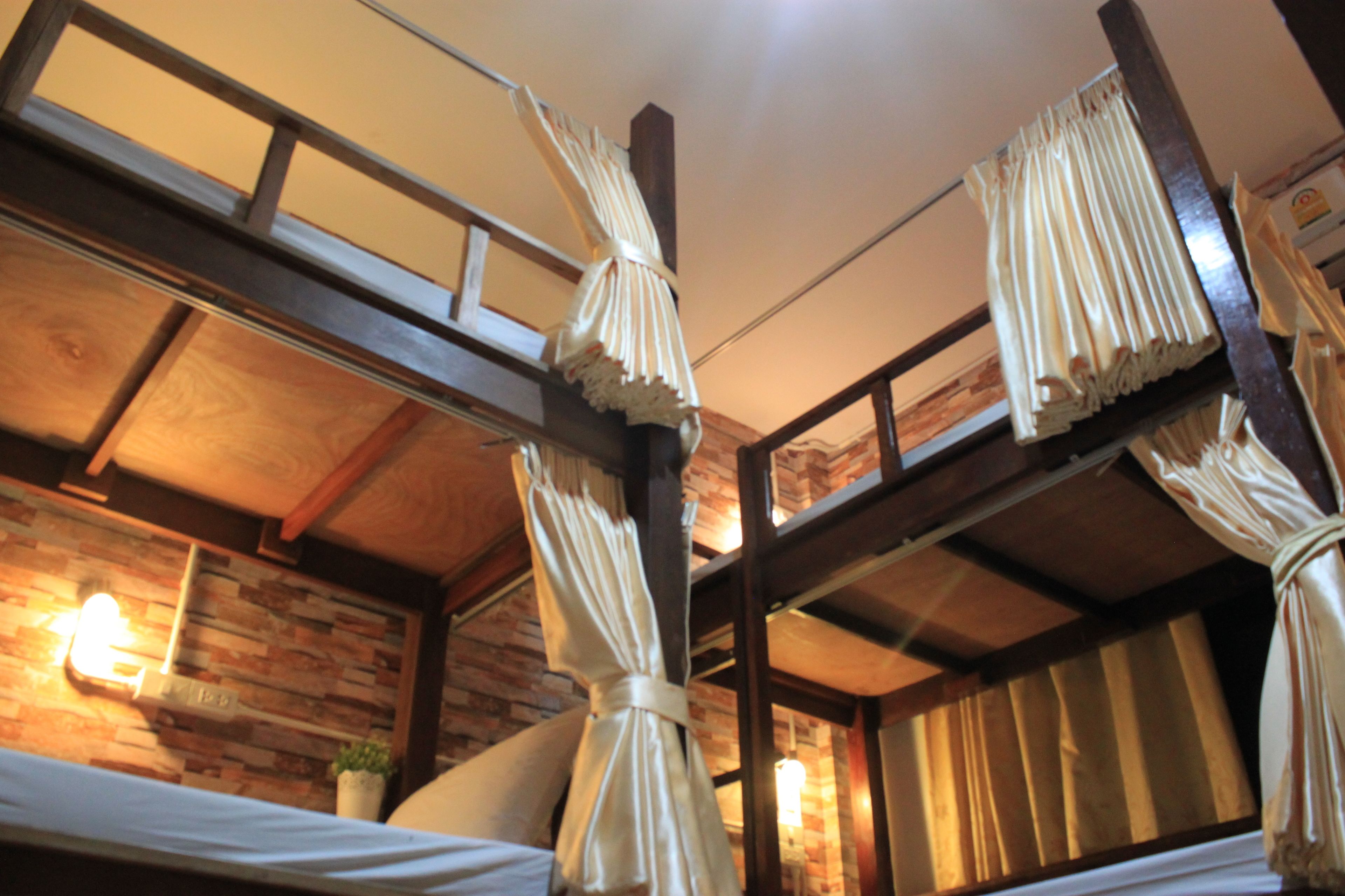 A room with a wooden ceiling, a brick wall, and a bed with curtains.