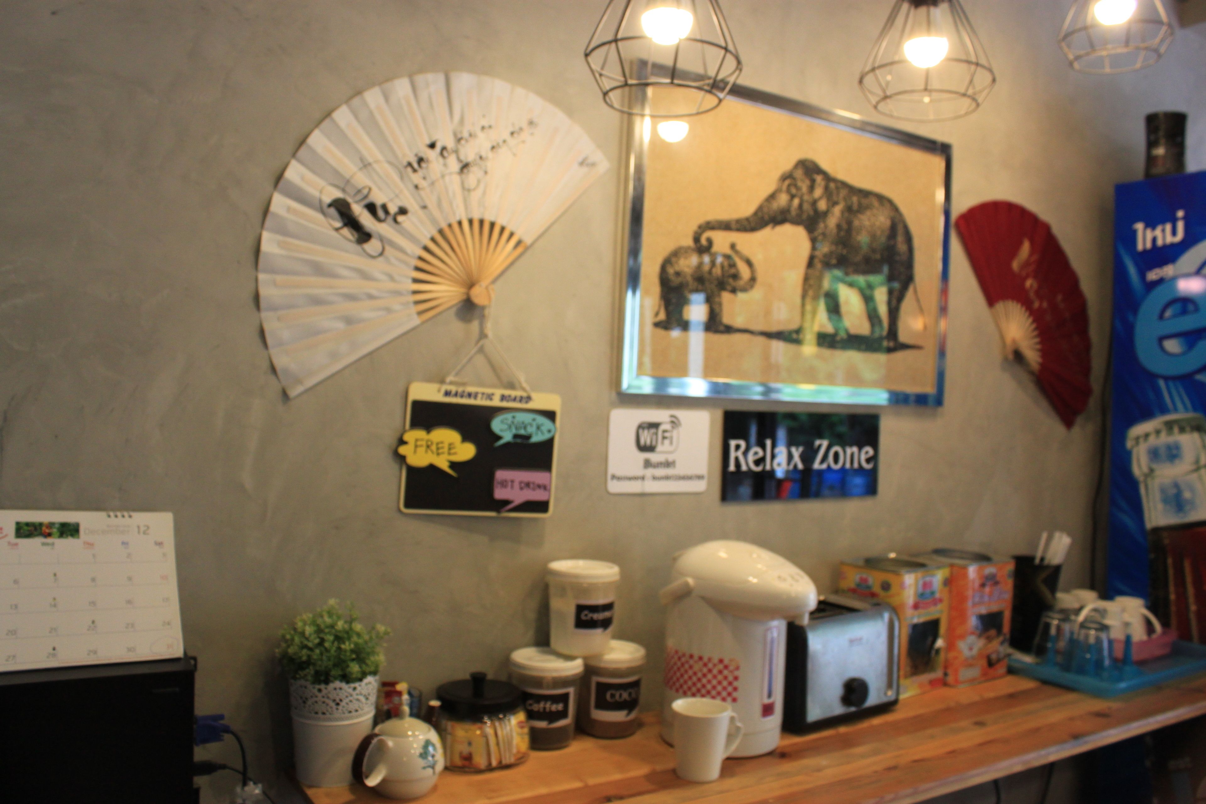 A wall with a calendar, a fan, a coffee maker, and a framed picture of elephants.