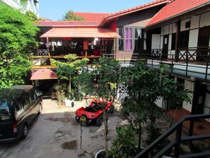 A courtyard with a red car, a black van, and a building with a red roof and white walls.