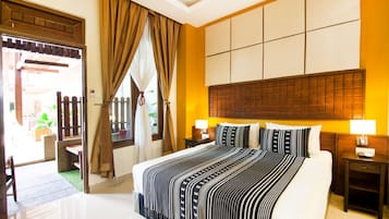 A hotel room with a large bed, two bedside tables with lamps, a wooden headboard, and a view of the outside through a door with curtains.