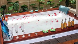 Eine mit Wasser und Rosenblättern gefüllte Badewanne, umgeben von Pflanzen und Kerzen.