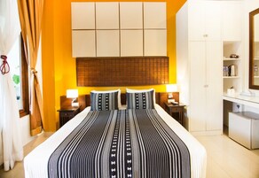Una habitación de hotel con una cama grande, cabecera con diseño de panel, dos mesitas de noche con lámparas, un armario y una pequeña kitchenette.