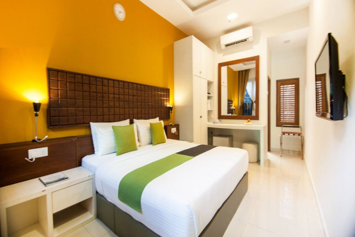 A hotel room with a large bed, a desk, a mirror, and an air conditioning unit.