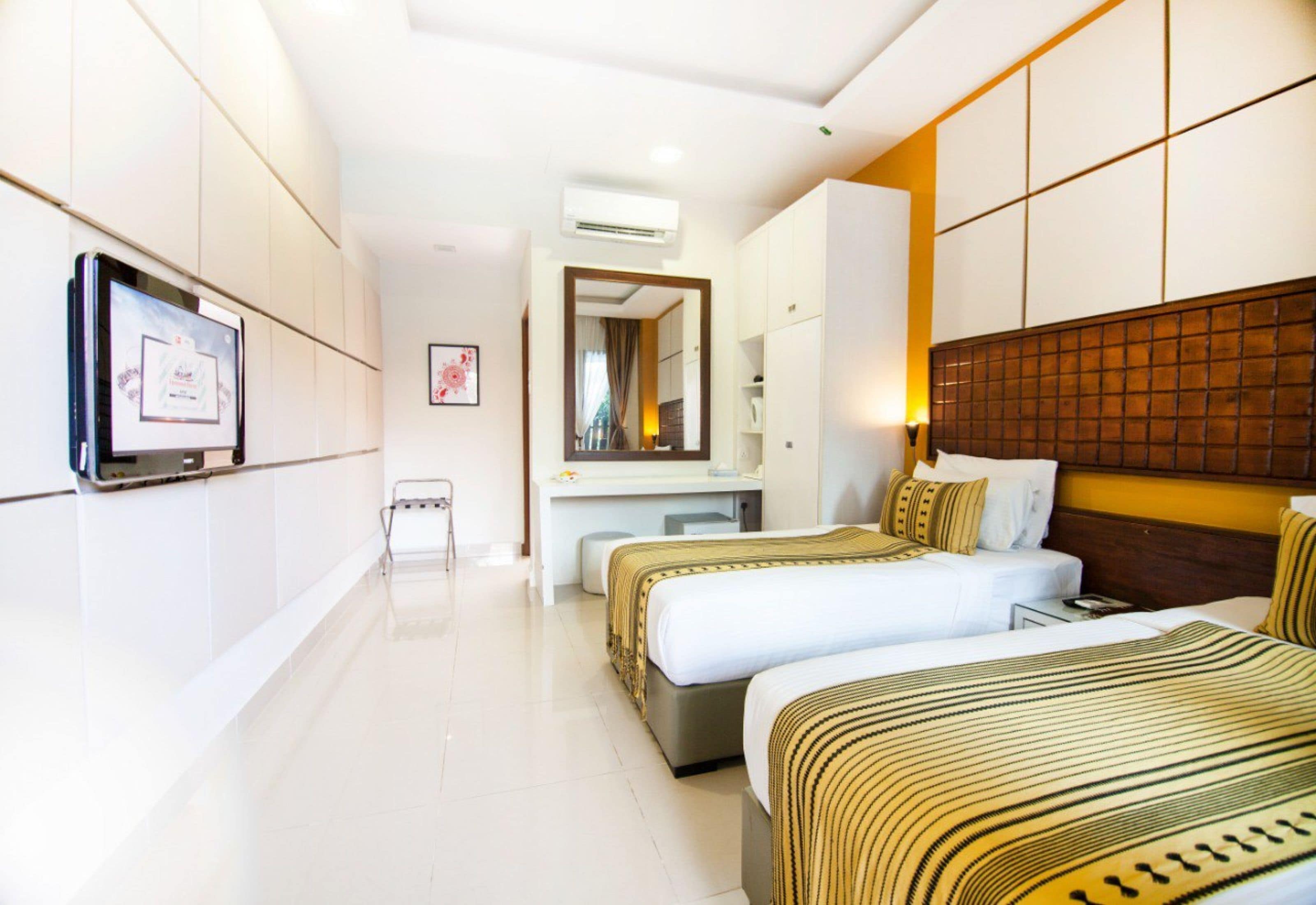 A hotel room with two beds, a desk, a TV, and a large mirror.