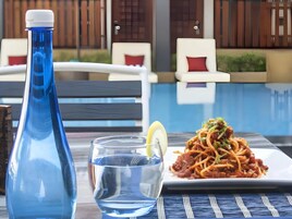 A dining table with a plate of spaghetti, a glass of water, and a blue water bottle.