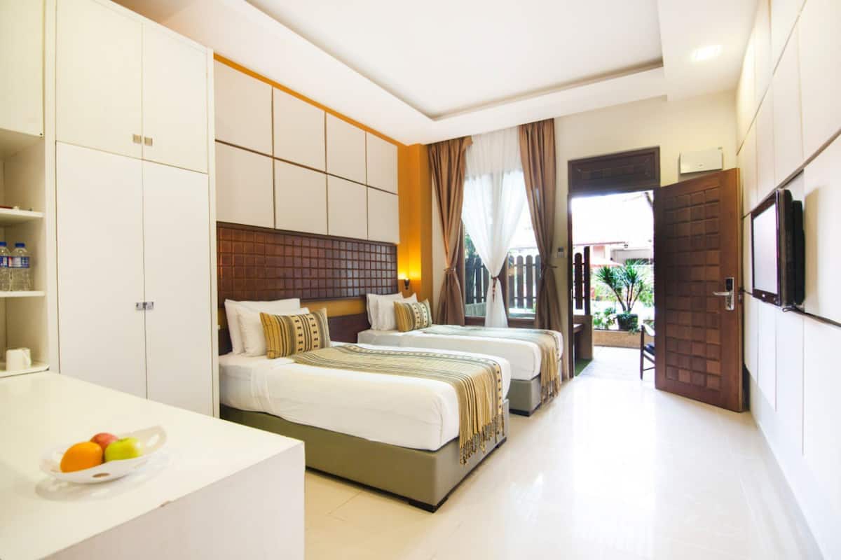 A hotel room with two beds, a desk with a fruit bowl, a TV, and a view of the outdoors.
