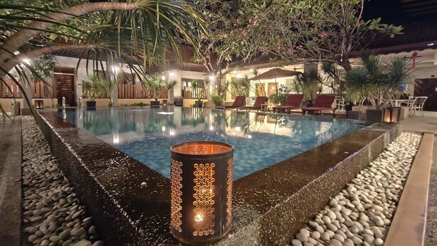 Ein Poolbereich bei Nacht mit klarem Wasser, umgebenden Pflanzen und einer Kerze.