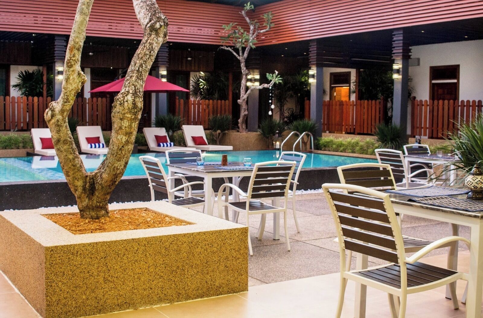 A poolside area with lounge chairs, a table, and a decorative tree.