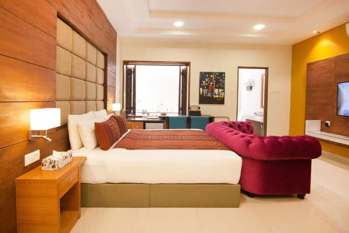 A modern hotel room with a large bed, a desk, a television, and a comfortable armchair.