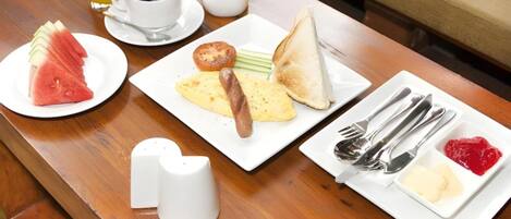 A breakfast table with plates of toast, eggs, sausage, and fruit, along with cups of coffee and orange juice.
