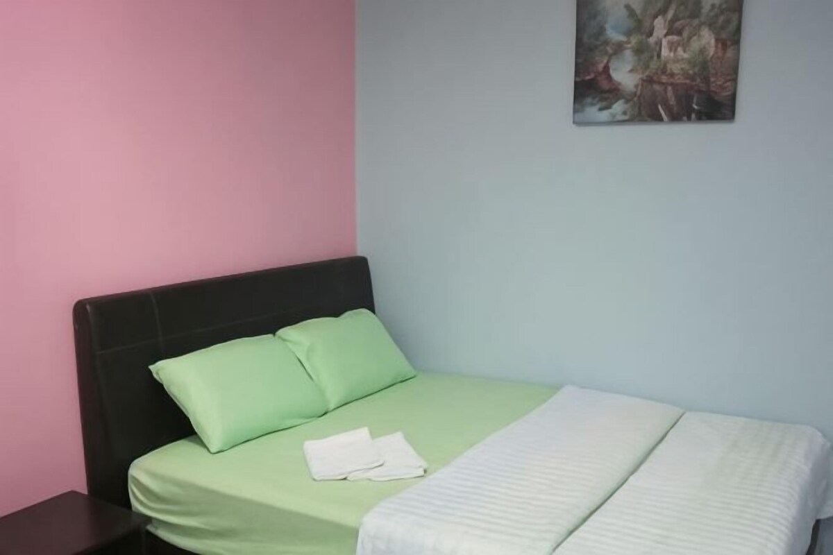 A bed with green and white bedding, a black headboard, and a painting on the wall.