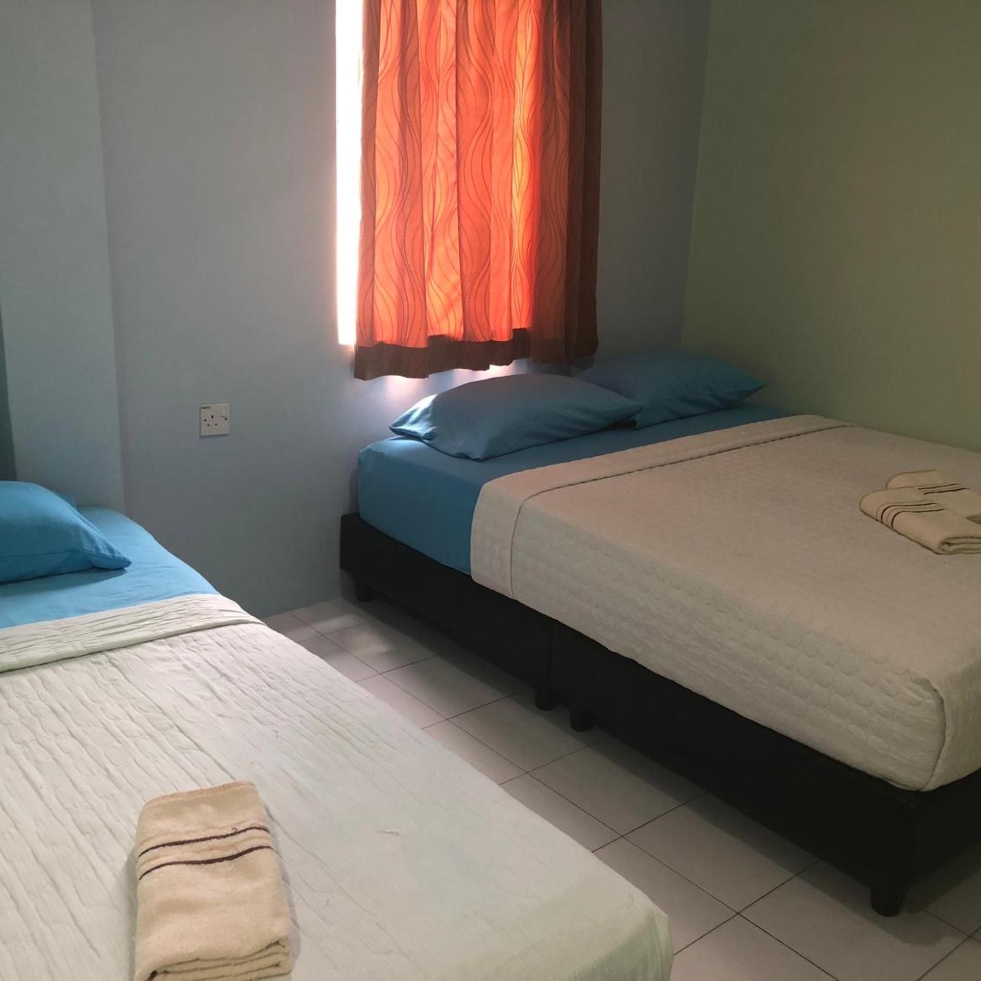 A room with two beds, one with a blue bedspread and the other with a white bedspread.