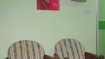 Two wicker armchairs with striped fabric against a light-colored wall, a red floral painting above them, and a green door in the background.