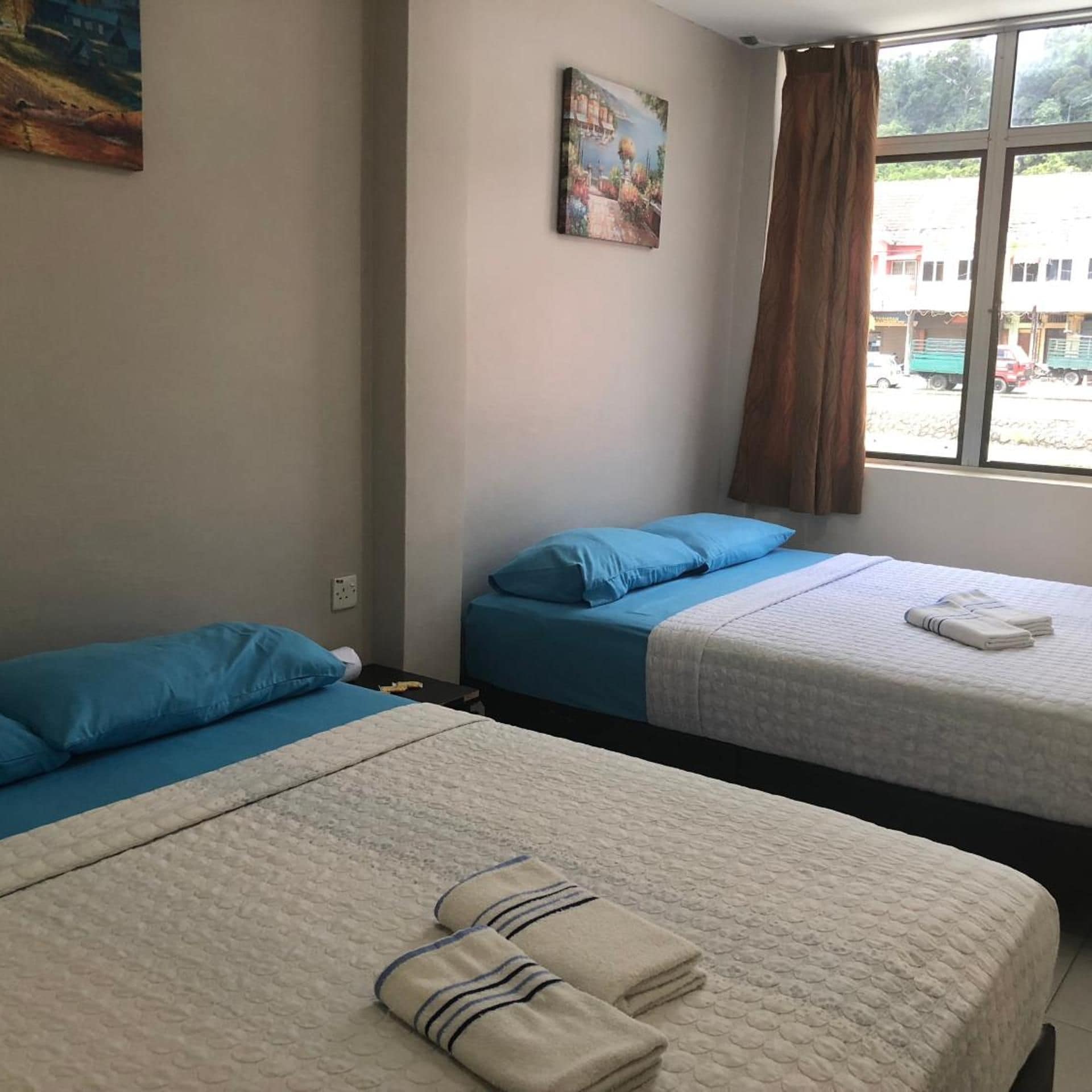 Ein Hotelzimmer mit zwei Betten, einem Bild an der Wand und Blick auf die Straße durch das Fenster.