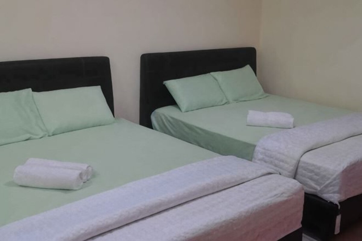 Two twin beds with green bedding and white towels, a black headboard, and a plain wall.