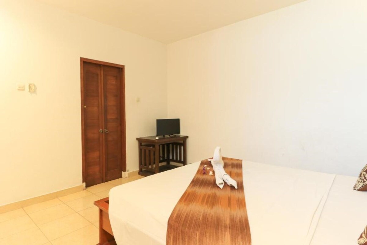 A hotel room with a bed, a wooden nightstand, a television, and a door.