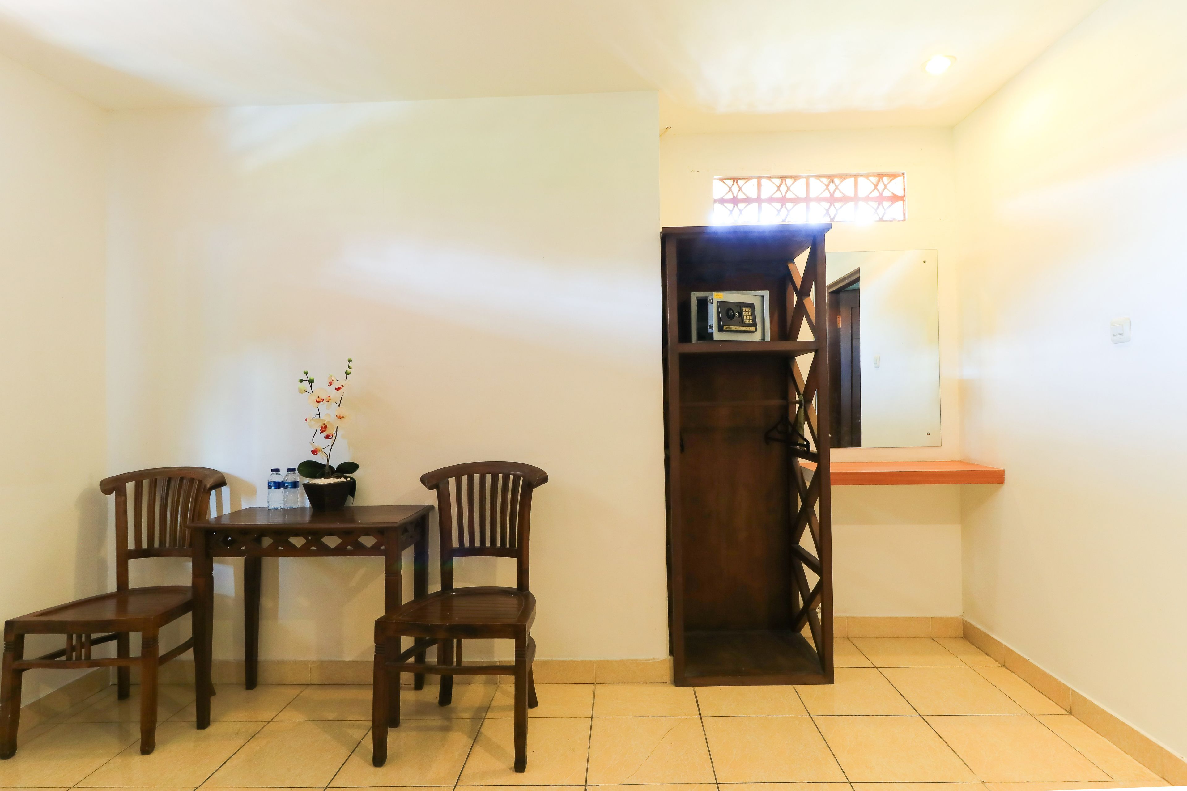 Una habitación pequeña y luminosa con una mesa de madera y dos sillas, una planta en maceta y un estante con algunos objetos.