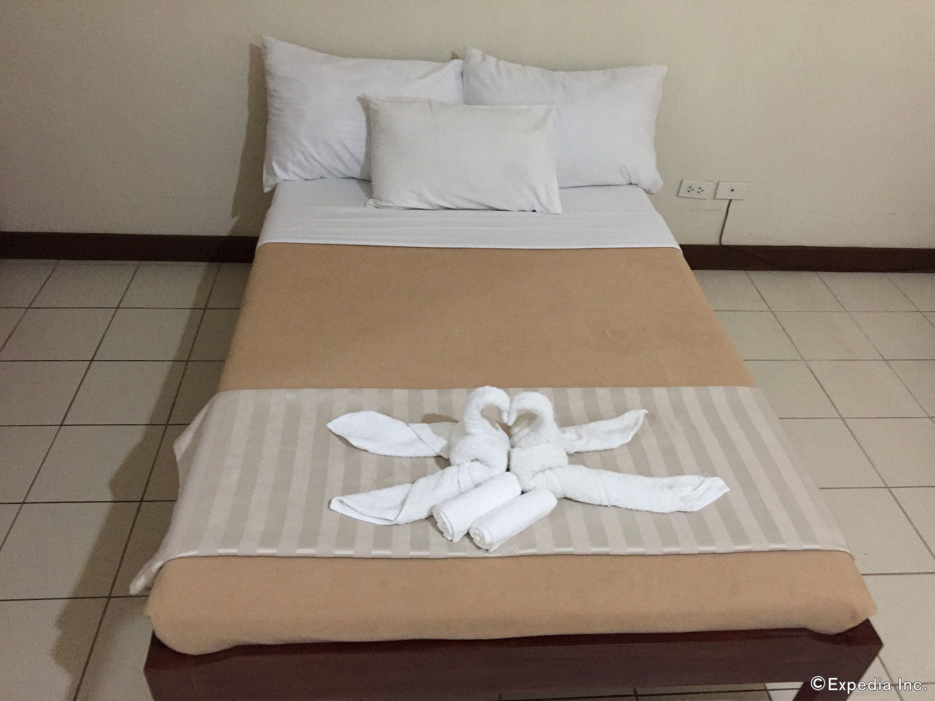Une chambre d’hôtel avec un lit, des oreillers blancs, une couverture à rayures et une serviette disposée en forme de cœur sur le lit.