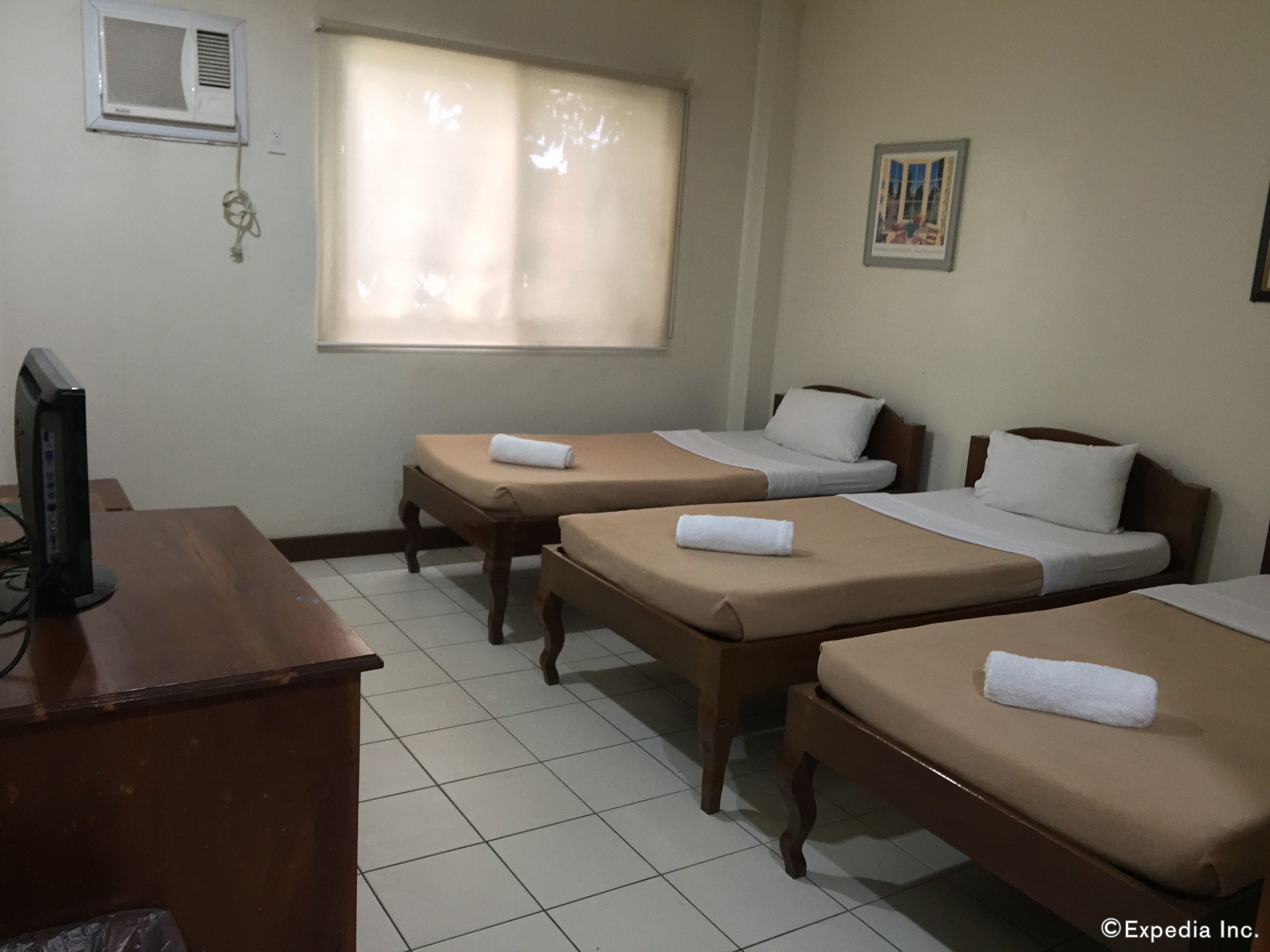 Habitación de hotel con dos camas individuales, un escritorio de madera con una computadora, una ventana con persianas y un aire acondicionado de pared.