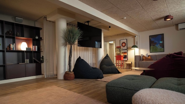 Una sala de estar moderna con piso de madera, un televisor de pantalla plana, una estantería y un rincón de estar acogedor con cojines.