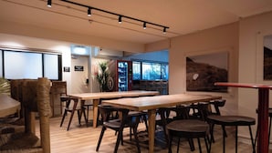 Un comedor moderno con mesas y sillas de madera, una máquina expendedora y un ventanal con vistas a un paisaje montañoso.