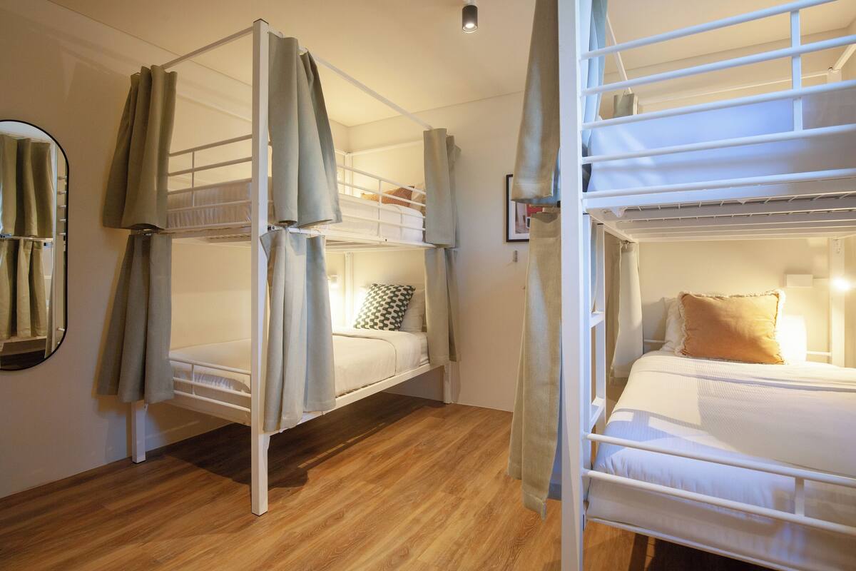 Una habitación con dos literas, piso de madera, un espejo y cortinas.