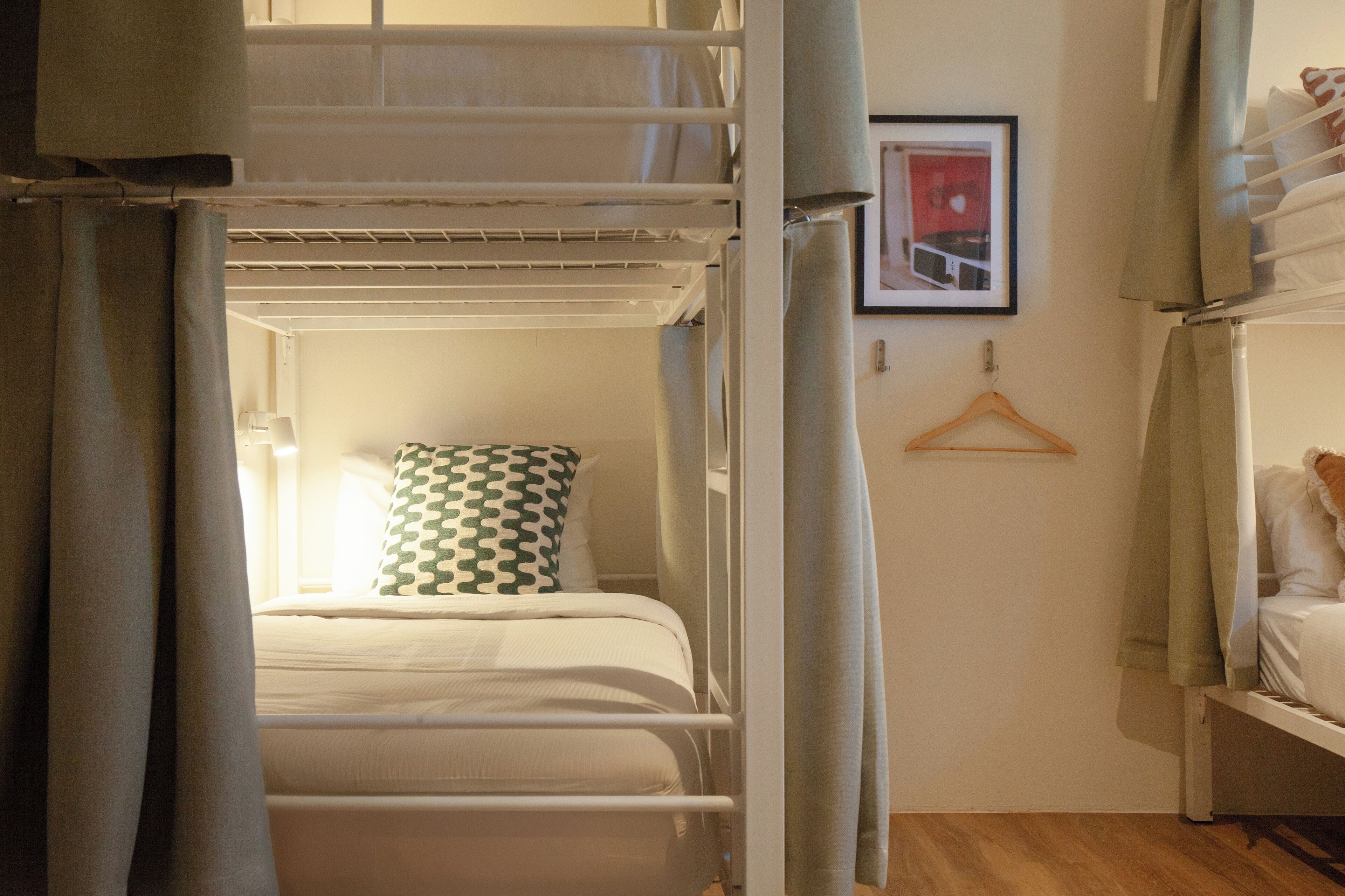 A bunk bed room with a window, a hanging coat rack, and a framed picture on the wall.