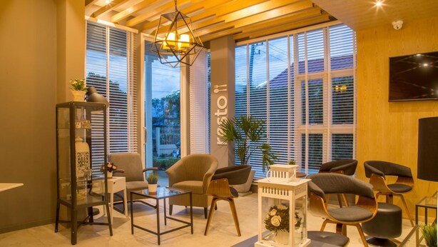 Un salon moderne avec des poutres en bois au plafond, de grandes fenêtres équipées de stores et divers éléments de mobilier, notamment un canapé, des fauteuils et une table basse.