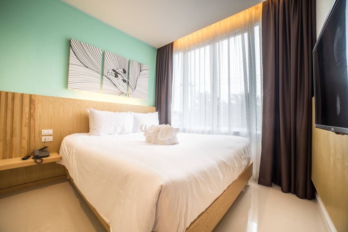 A hotel room with a large bed, a bedside table with a phone, and a window with curtains.