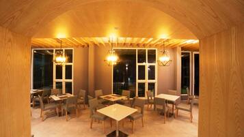 A cozy restaurant with wooden walls and ceiling, featuring multiple tables and chairs, and large windows allowing natural light.