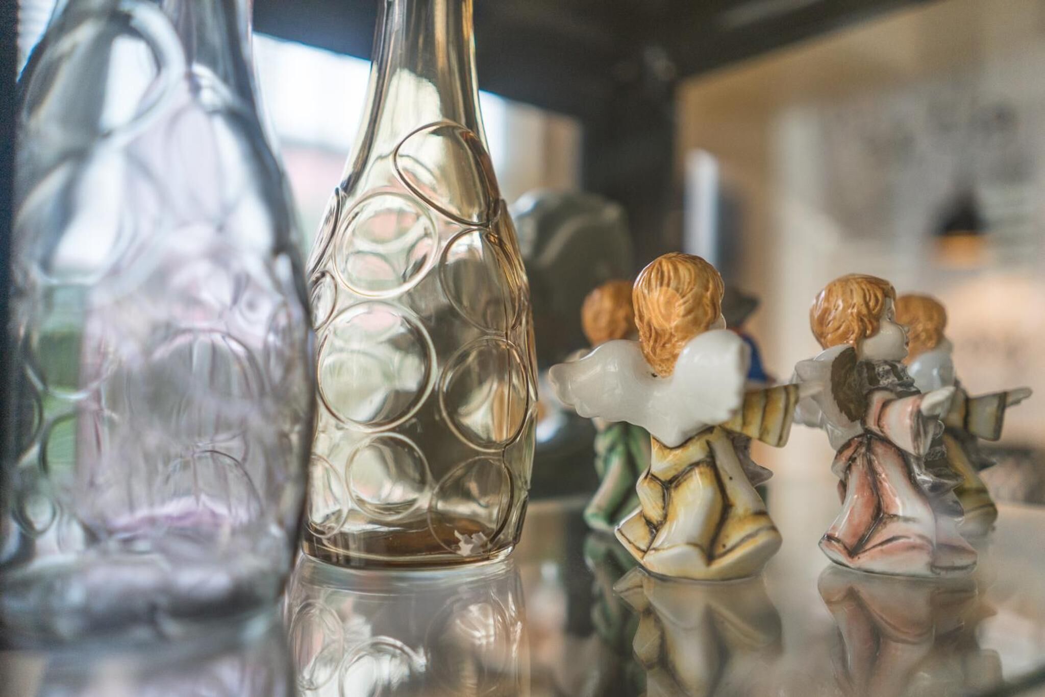 A clear glass bottle with a reflective surface, a decorative figurine, and a blurred background.