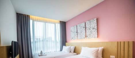 Habitación de hotel con dos camas, un televisor de pantalla plana, una mesita de noche con teléfono y un ventanal con cortinas.