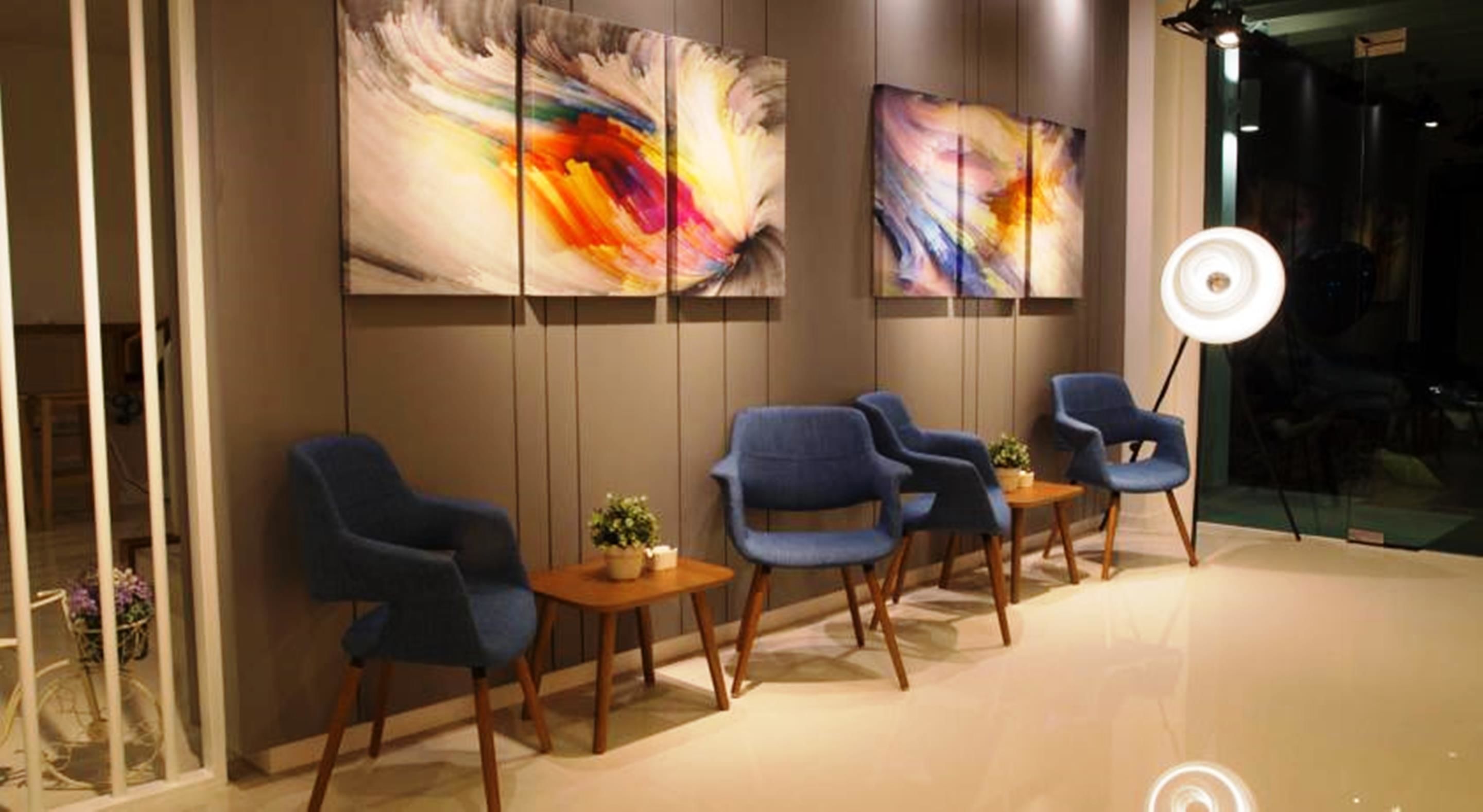 A modern waiting area with blue chairs, a small table with a plant, and abstract art on the wall.
