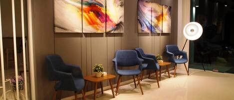 A modern waiting area with blue chairs, a small table with a plant, and abstract art on the wall.