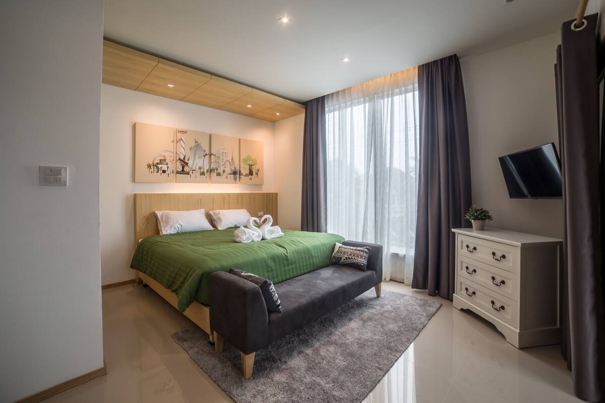 A modern bedroom with a bed, a sofa, a TV, and artwork on the wall.
