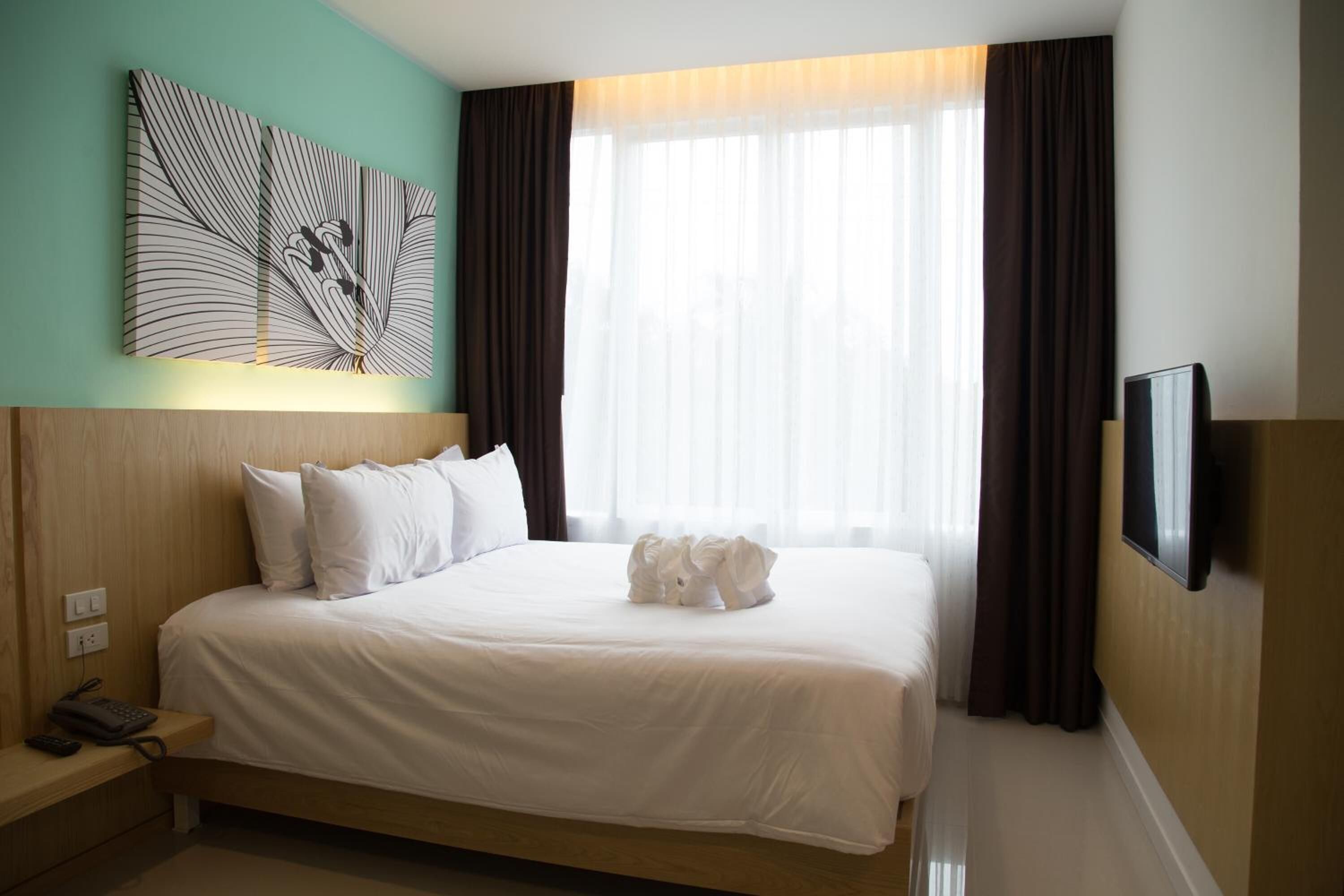 Een hotelkamer met een bed, een tv aan de muur, een schilderij en een raam met gordijnen.